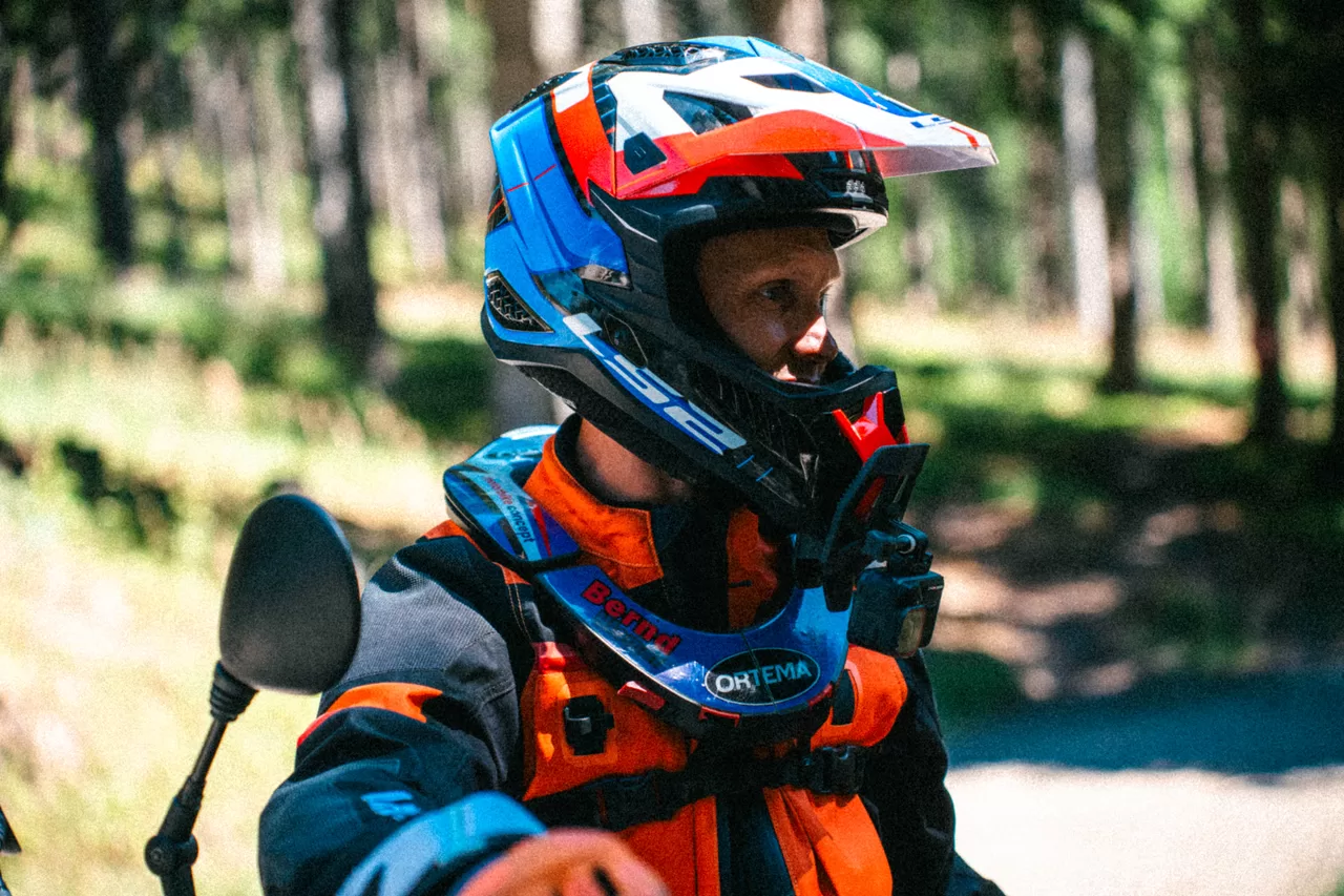 Porträt eines Offroad-Fahrers in orange-blauer Ausrüstung neben den KTM-Motorrädern