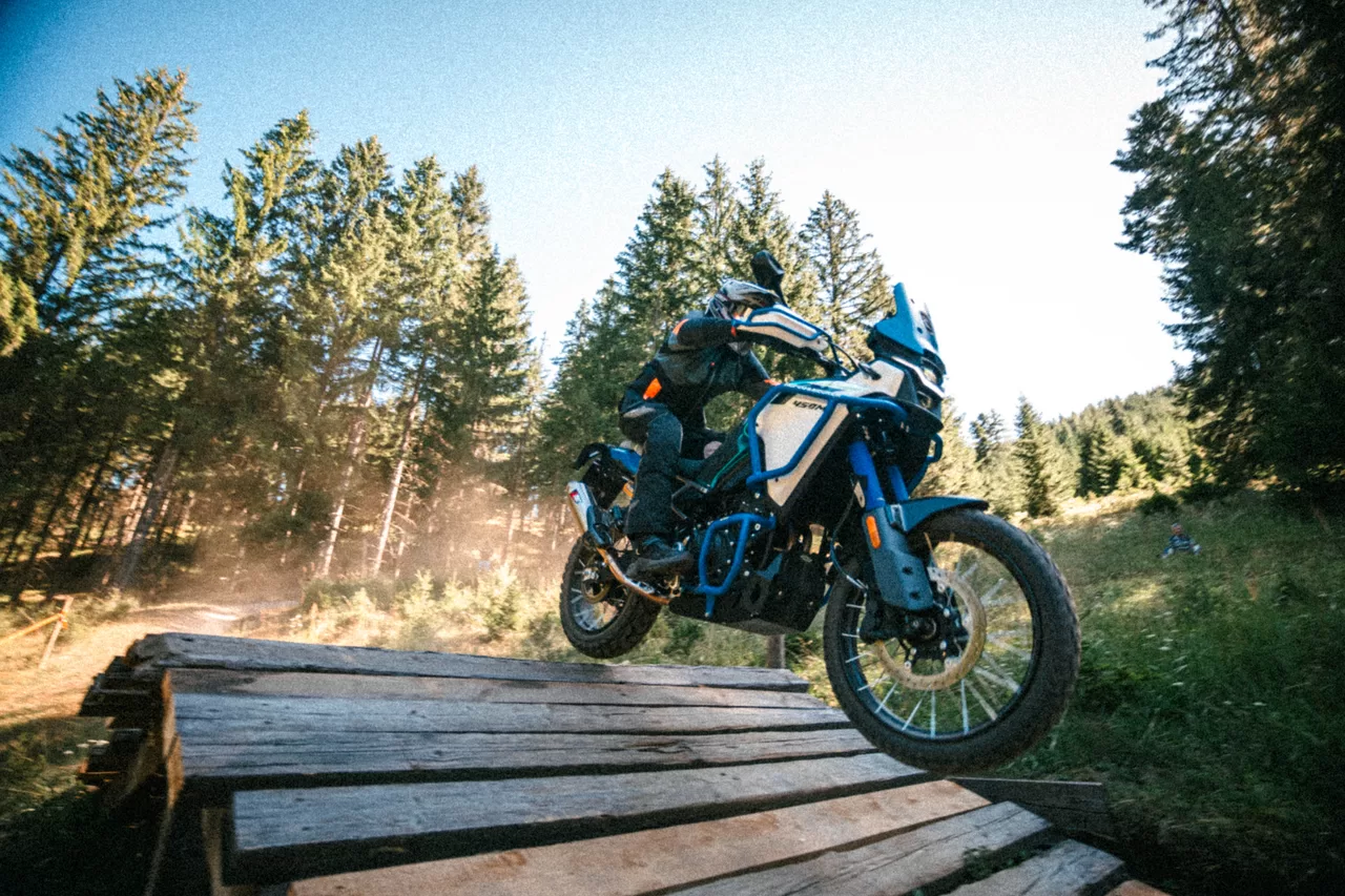 Blaues Adventure-Motorrad beim Sprung über eine hölzerne Offroad-Rampe